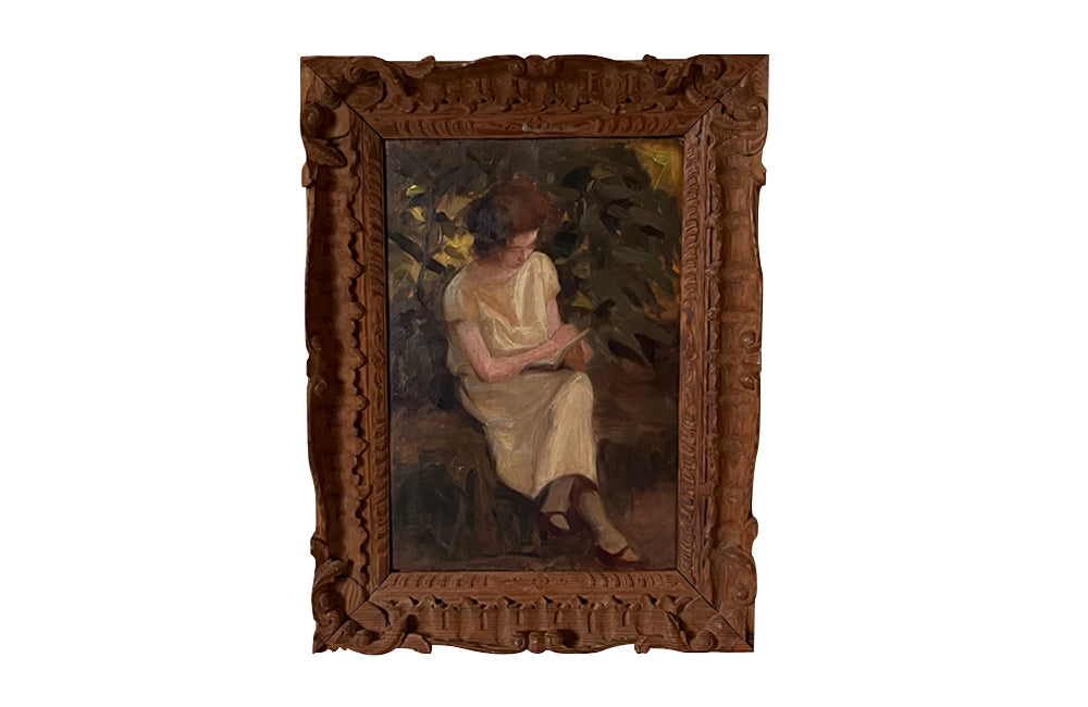 Charming framed oil on wood painting of a seated young woman reading in her garden .