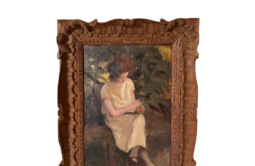 Charming framed oil on wood painting of a seated young woman reading in her garden .
