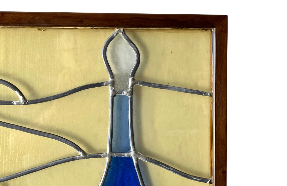 Framed stained glass still-life of a basket of vegetable and wine bottle.