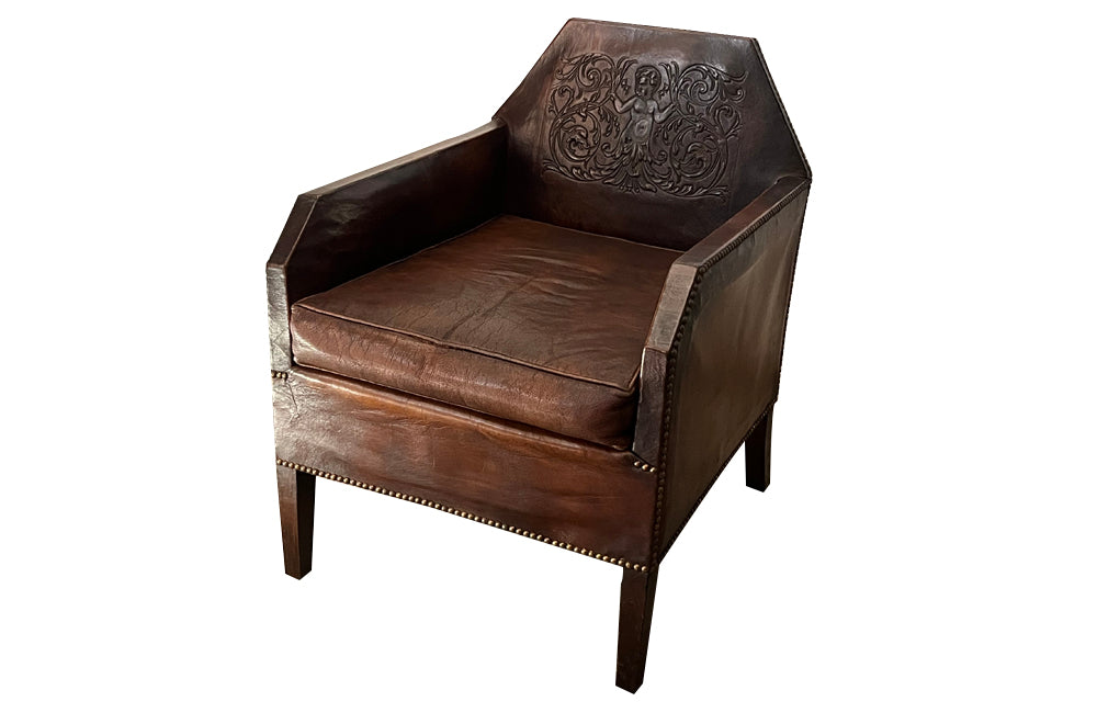 Antique club chair leather with embossed back featuring a putti and scrolled foliate decoration. France.