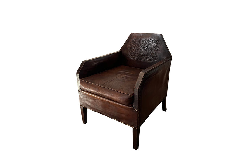 Antique club chair leather with embossed back featuring a putti and scrolled foliate decoration. France.