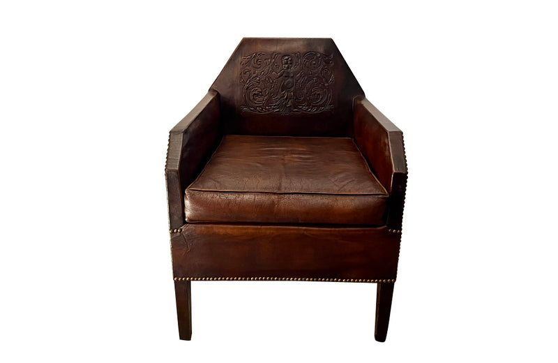 Antique club chair leather with embossed back featuring a putti and scrolled foliate decoration. France.