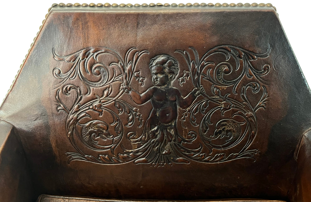 Antique club chair leather with embossed back featuring a putti and scrolled foliate decoration. France.