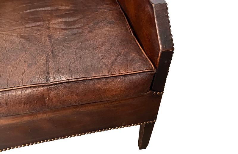 Antique club chair leather with embossed back featuring a putti and scrolled foliate decoration. France.