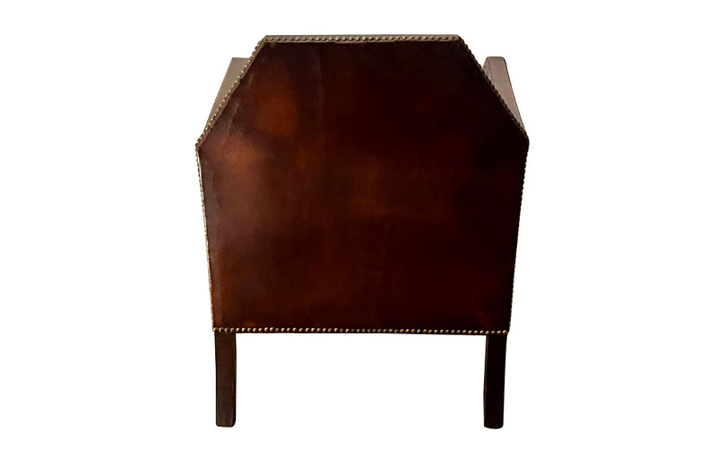 Antique club chair leather with embossed back featuring a putti and scrolled foliate decoration. France.
