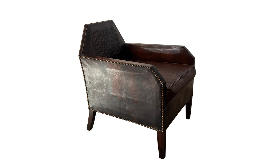 Antique club chair leather with embossed back featuring a putti and scrolled foliate decoration. France.