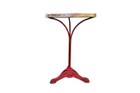 A pedestal table with a distressed red cast iron tripod base and a circular marble top 