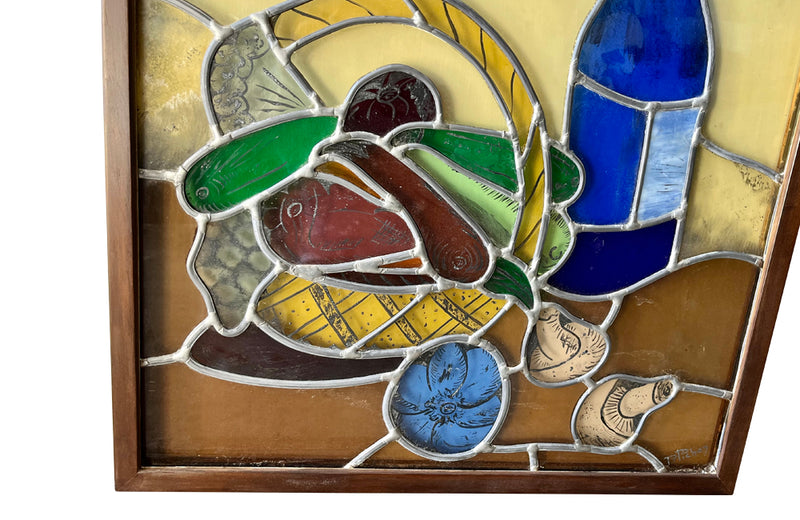 Framed stained glass still-life of a basket of vegetable and wine bottle.