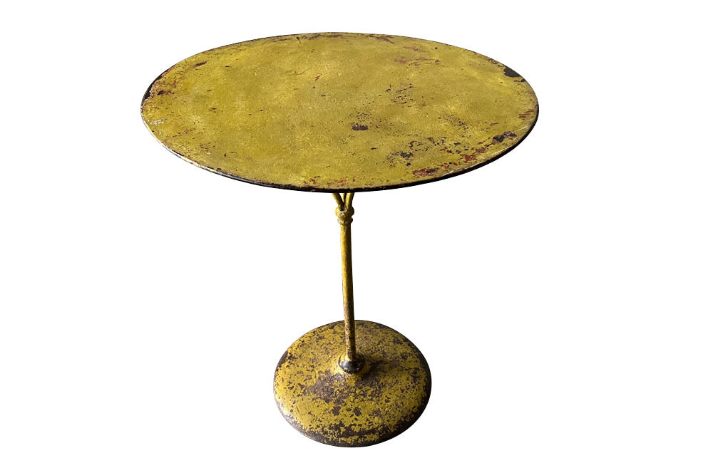 French antique round iron garden table with lovely old yellow paint and three elegant downrights joining to form one stem terminating on a heavy round base