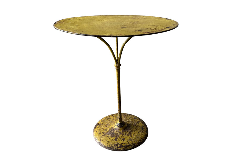 French antique round iron garden table with lovely old yellow paint and three elegant downrights joining to form one stem terminating on a heavy round base